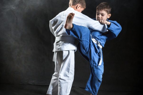 Two elementary aged boys are practicing judo. The boys dressed in sport uniforms judo gi. They are performing training judo fight. Studio shooting in light haze on black background